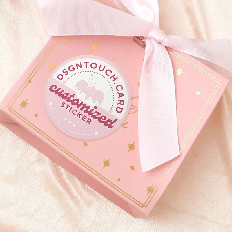 Customized "DSGNTouch" sticker for gift packaging: pink & gold design (with unicorn graphic) applied to a star-accented pink gift box, tied with a satin ribbon.
