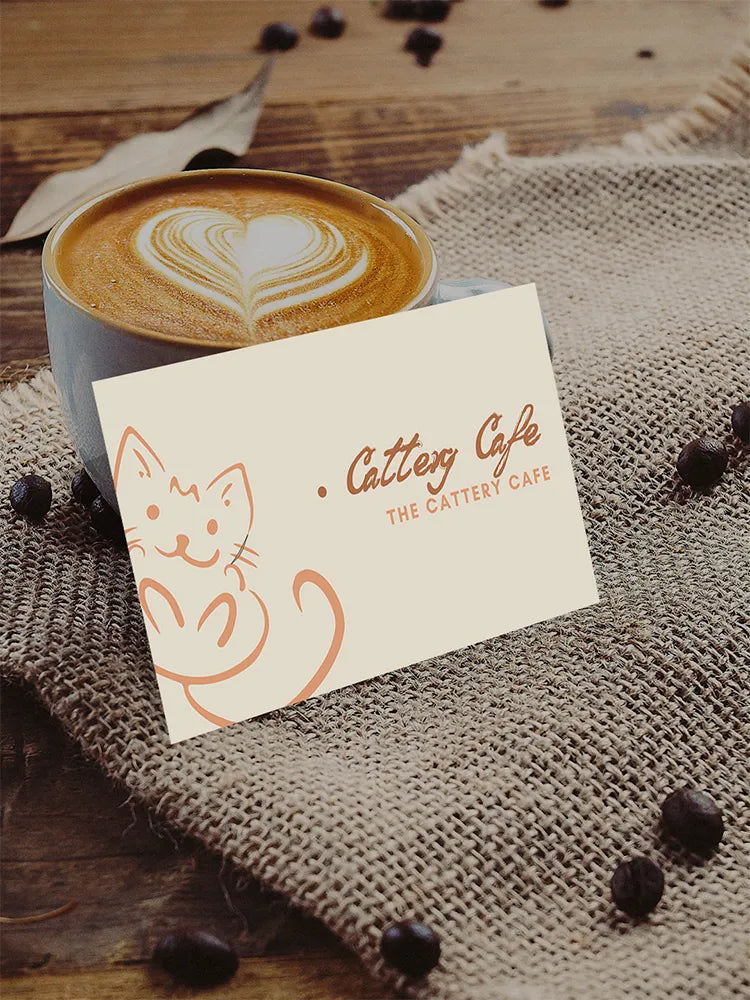 Coffee cup with latte art next to Cattery Cafe loyalty card on burlap surface.